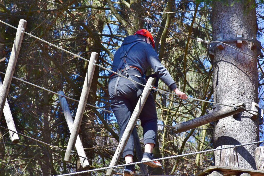 Ein Kletterer im Abenteuerpark testet seine Balance auf Holzbalken, ein beliebtes Aktiv-Ausflugsziel in Niedersachsen.